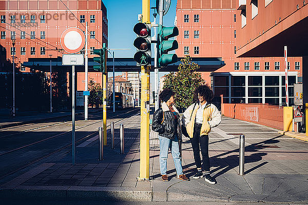 Zwei coole junge Freundinnen unterhalten sich am Fußgängerüberweg
