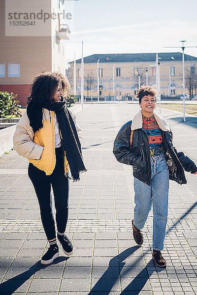 Zwei coole junge Freundinnen gehen und unterhalten sich auf dem städtischen Bürgersteig