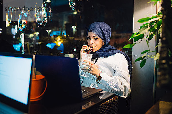 Junge Frau im Hijab trinkt Smoothie im Café