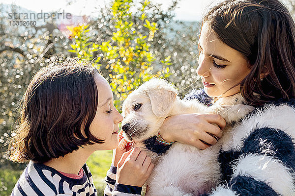 Zwei Mädchen halten und streicheln einen süßen Golden Retriever-Welpen im Obstgarten  Scandicci  Toskana  Italien