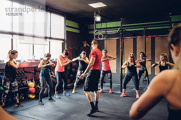 Gruppe von Frauen  die mit einem männlichen Trainer im Fitnessstudio trainieren  mit den Händen zusammen