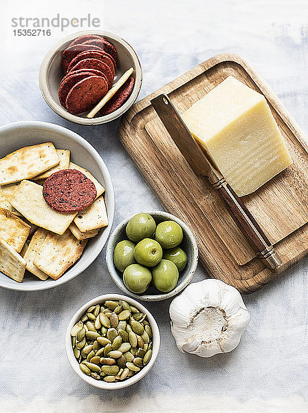 Stilleben von Schneidebrett und Käse mit Schalen mit Crackern  Oliven  Salami und Kürbiskernen  Draufsicht