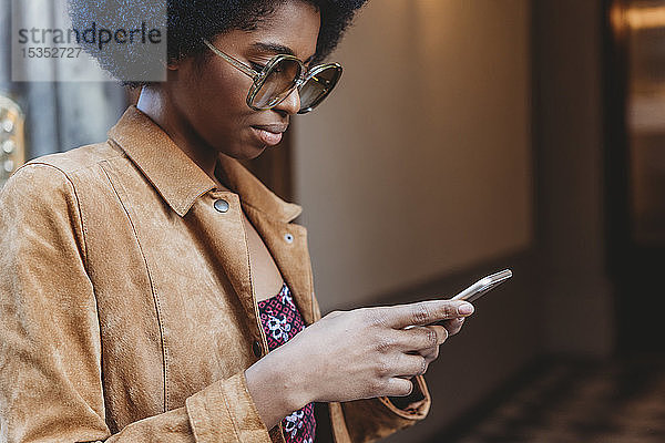 Junge Frau mit Afro-Haaren benutzt Smartphone vor dem Gebäude