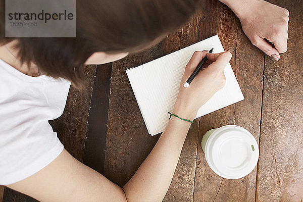 Frau schreibt in der Kaffeepause auf ein Notizbuch