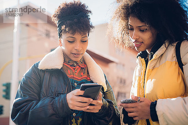 Zwei coole junge Frauen schauen sich auf dem städtischen Bürgersteig ein Smartphone an