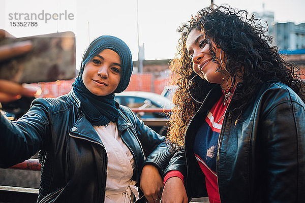 Junge Frau im Hidschab und Freundin posieren für Selfie in der Stadt