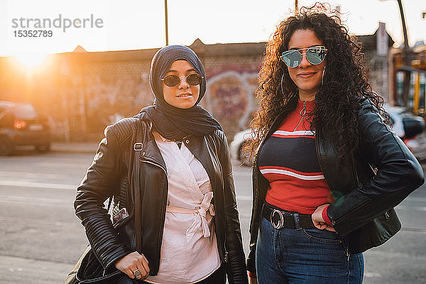 Junge Frau im Hidschab und beste Freundin in der Stadt bei Sonnenuntergang  Porträt