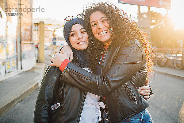 Junge Frau im Hidschab und beste Freundin umarmen sich in der Stadt  Porträt