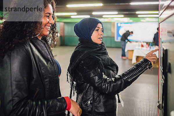 Junge Frau im Hidschab und Freundin kaufen Fahrkarten in der U-Bahn-Station