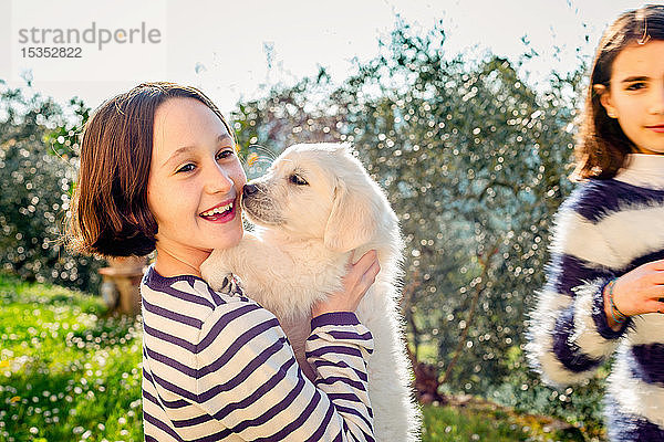 Mädchen und ihre Freundin halten einen süßen Golden Retriever-Welpen im Obstgarten  Scandicci  Toskana  Italien