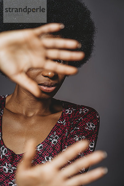 Junge Frau mit Afrohaaren  die das Gesicht mit Händen bedeckt  grauer Hintergrund