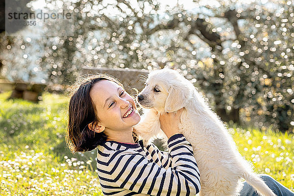 Mädchen sitzt im Obstgarten und spielt mit einem süßen Golden Retriever-Welpen  Scandicci  Toskana  Italien