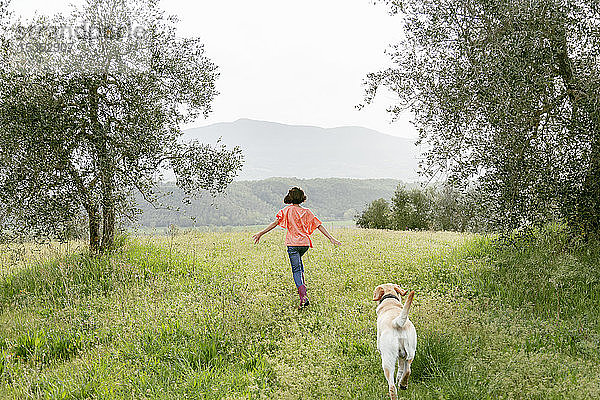Mädchen rennt mit Labradorhund in malerischer Feldlandschaft  Rückansicht  Citta della Pieve  Umbrien  Italien