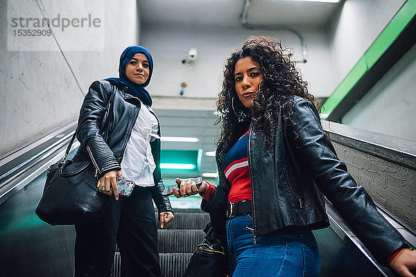 Junge Frau im Hidschab mit Freundin fährt U-Bahn-Rolltreppe hoch