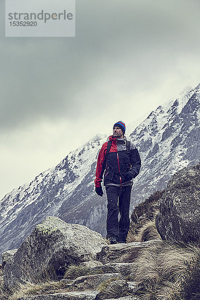 Männlicher Wanderer wandert in zerklüfteter Landschaft mit schneebedeckten Bergen  Llanberis  Gwynedd  Wales