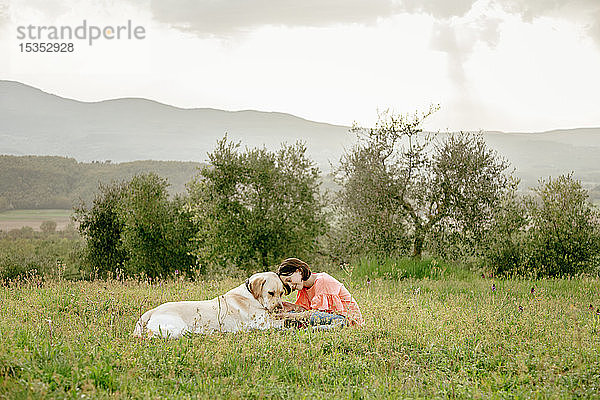 Mädchen sitzt und streichelt Labradorhund in malerischer Feldlandschaft  Citta della Pieve  Umbrien  Italien