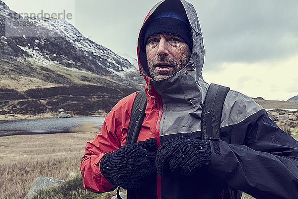 Männlicher Wanderer mit Kapuze oben in schneebedeckter Berglandschaft  Porträt  Llanberis  Gwynedd  Wales