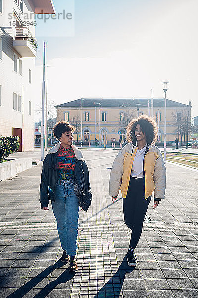 Zwei coole junge Freundinnen schlendern auf dem städtischen Bürgersteig  in voller Länge