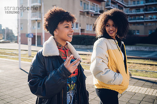 Zwei junge Frauen gehen und sprechen auf dem städtischen Bürgersteig
