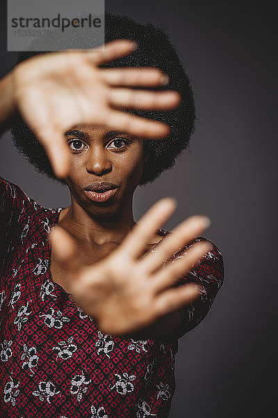 Junge Frau mit Afrohaaren  die das Gesicht mit Händen bedeckt  grauer Hintergrund