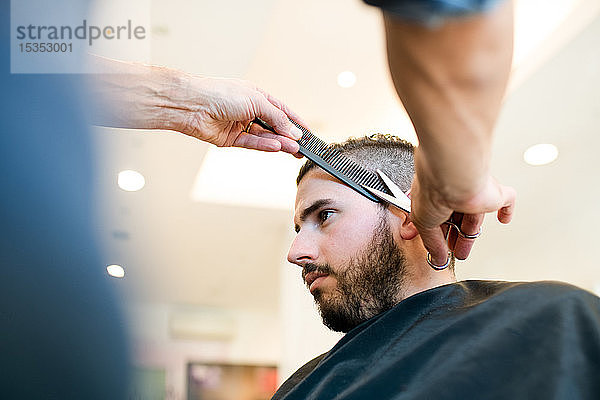 Friseur schneidet Kunden in Friseursalon die Haare