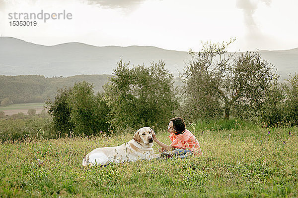 Mädchen sitzt und streichelt Labradorhund in malerischer Feldlandschaft  Citta della Pieve  Umbrien  Italien