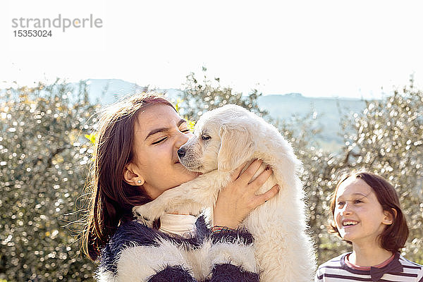 Mädchen mit ihrer Freundin hält einen süßen Golden Retriever-Welpen im Obstgarten hoch  Scandicci  Toskana  Italien