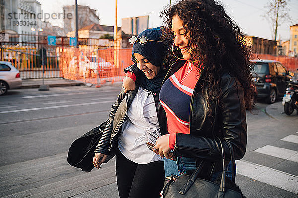 Junge Frau im Hidschab und beste Freundin gehen und reden in der Stadt