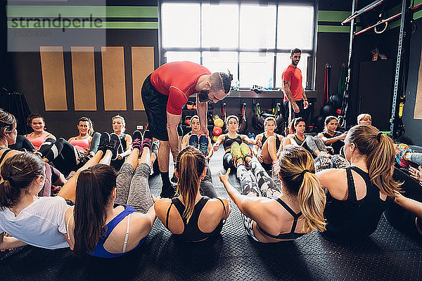 Frauen trainieren im Fitnessstudio mit männlichen Trainern  die mit angehobenen Beinen auf dem Boden sitzen