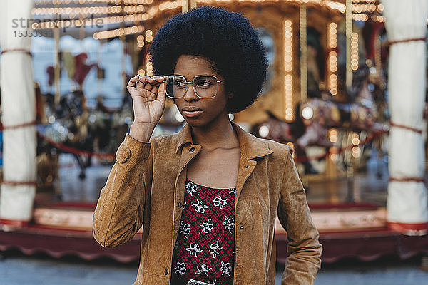 Junge Frau mit Afro-Haaren setzt vor dem Karussell eine Brille auf