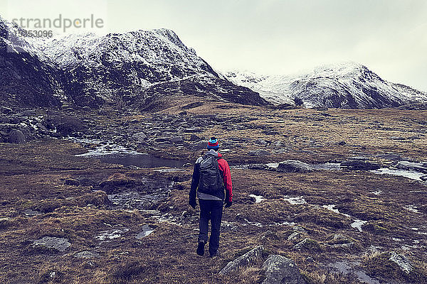 Männlicher Wanderer mit Blick auf zerklüftete Landschaft mit schneebedeckten Bergen  Rückansicht  Llanberis  Gwynedd  Wales
