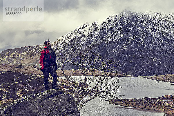 Männlicher Wanderer mit Blick auf See und schneebedeckte Berglandschaft  Llanberis  Gwynedd  Wales