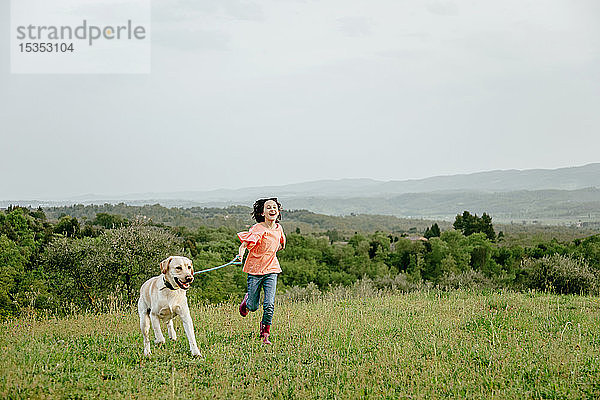 Mädchen rennt mit Labradorhund in malerischer Feldlandschaft  Citta della Pieve  Umbrien  Italien
