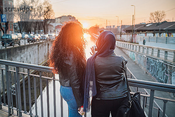 Junge Frau im Hidschab und beste Freundin fotografieren Kanal bei Sonnenuntergang in der Stadt
