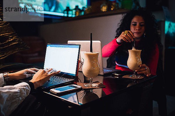 Zwei Frauen am Café-Tisch  die Smoothie trinken und am Laptop tippen