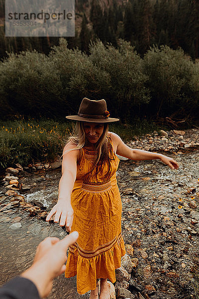 Schwangere Frau in orangefarbenem Maxikleid  die aus ländlichem Fluss nach der Hand greift  Mineral King  Kalifornien  USA