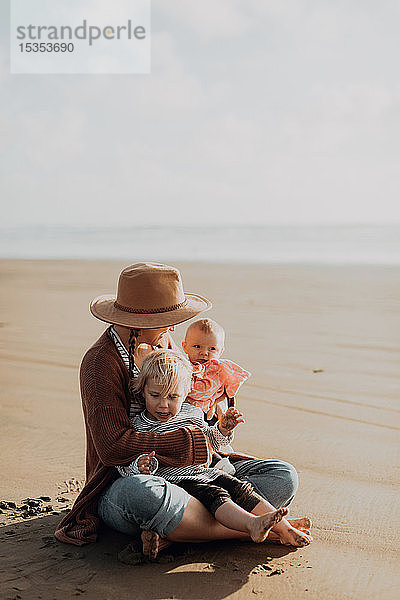 Mutter und Kinder am Strand sitzend