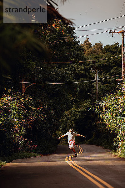 Mittelgroßer erwachsener männlicher Skateboarder  der auf der Mittellinie entlang einer Landstraße skateboard fährt  Haiku  Hawaii  USA