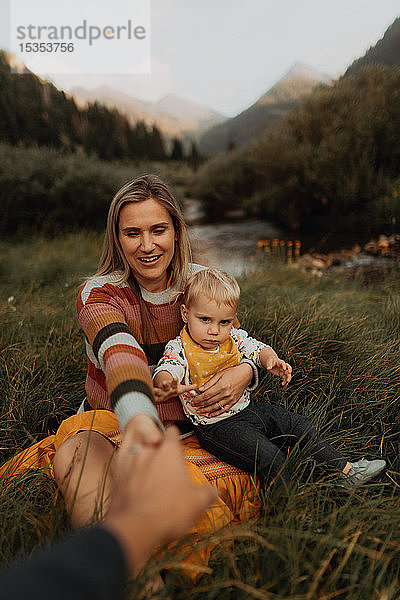 Mittelgroßes erwachsenes Paar mit Kleinkind-Tochter am ländlichen Fluss sitzend und Händchen haltend  Mineral King  Kalifornien  USA
