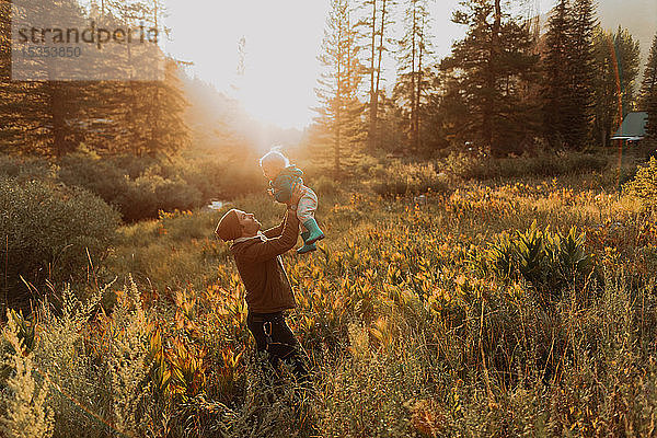 Mittelgroßer erwachsener Mann hält Kleinkind-Tochter im ländlichen Tal bei Sonnenuntergang hoch  Mineral King  Kalifornien  USA