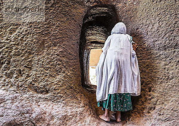 Äthiopische Frau beim Betreten eines in den Fels gehauenen Tunnels zwischen der Biete Medhane Alem (Haus des Erlösers der Welt) und der Biete Mariam (Haus der Maria)  äthiopisch-orthodoxe unterirdische Monolith-Felsenkirchen in der nördlichen Gruppe der in den Fels gehauenen Kirchen; Lalibela  Region Amhara  Äthiopien