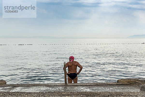 Männlicher Schwimmer steht und schaut auf die Küste und das Adriatische Meer; Opatija  Gespanschaft Primorje-Gorski Kotar  Kroatien