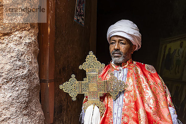 Priester  der ein kunstvolles Prozessionskreuz am Grab Adams in der Nordgruppe der Felsenkirchen hält; Lalibela  Amhara-Region  Äthiopien