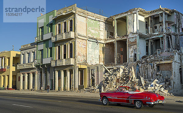 Ein altes Auto fährt an der abgerissenen Fassade eines alten Gebäudes entlang einer Straße vorbei; Havanna  Kuba