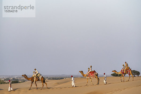 Menschen reiten mit Kamelen in der Wüste bei Sonnenuntergang; Rajasthan  Indien