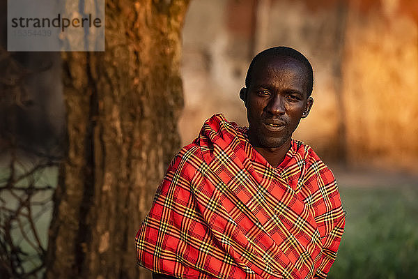 Nahaufnahme eines Massai-Mannes in Shuka an einem Baum; Tansania