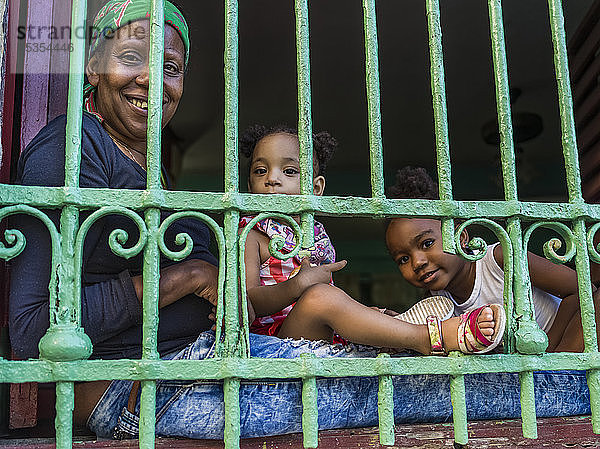 Eine Mutter mit zwei kleinen Töchtern sitzt da und schaut aus dem Gitter ihres Hauses; Havanna  Kuba