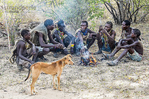 Hadzabe-Jäger und ihr Hund versammeln sich nach einer erfolgreichen Morgenjagd in der Nähe des Eyasi-Sees um ein Lagerfeuer; Tansania