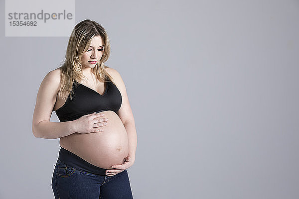 Eine junge schwangere Frau  die in einem Studio ihren Bauch hält und auf ihr ungeborenes Kind hinunterblickt; Edmonton  Alberta  Kanada