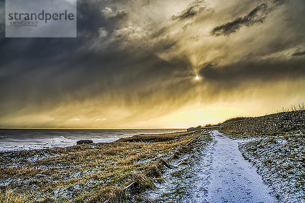 Schneebedeckter Weg entlang der Küstenlinie mit goldenem Sonnenlicht  das die Wolken beleuchtet; South Shields  Tyne and Wear  England